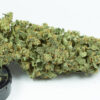 Close-up of a large cannabis bud with visible trichomes and orange pistils, resting on a black container labeled 'NAFEM SEED2 AUTO FLOWERING 3'.