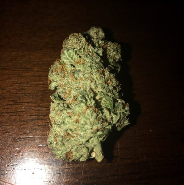 Von Barneys Farm Seeds Liberty Haze.Close-up of a detailed cannabis bud placed on a wooden surface, displaying a rich texture with visible crystals and orange hairs.